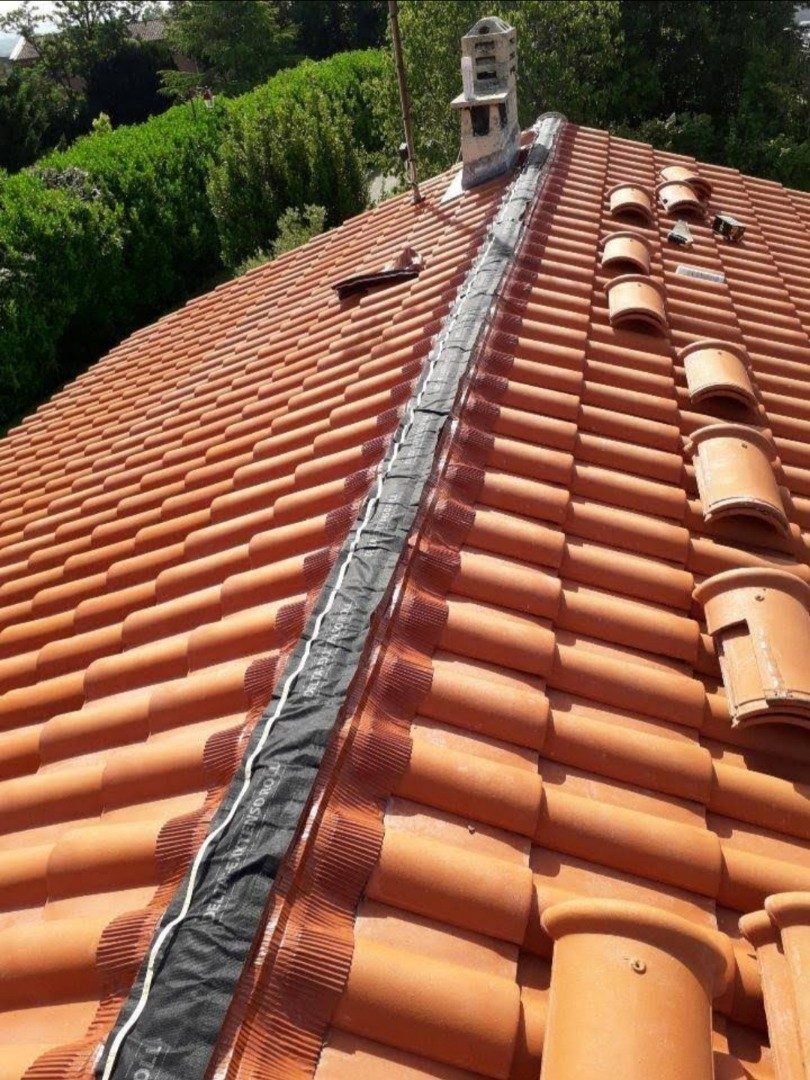 Faîtage en cours de réfection sur un toit en tuiles rouges, closoir neuf posé sous les tuiles faîtières.
