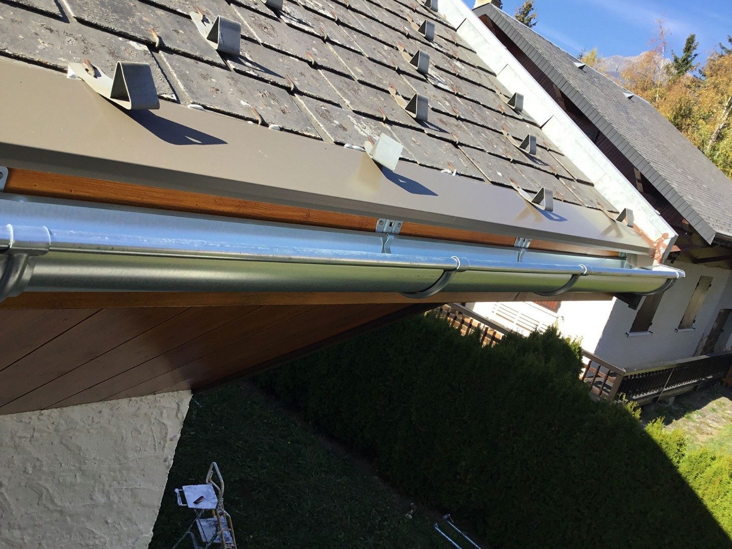 Gouttière neuve en aluminium posée sous une toiture en ardoises, avec son habillage de rive.